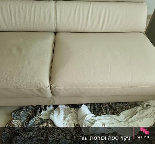 A beige leather sofa with a patterned cloth and white fabric on the floor.